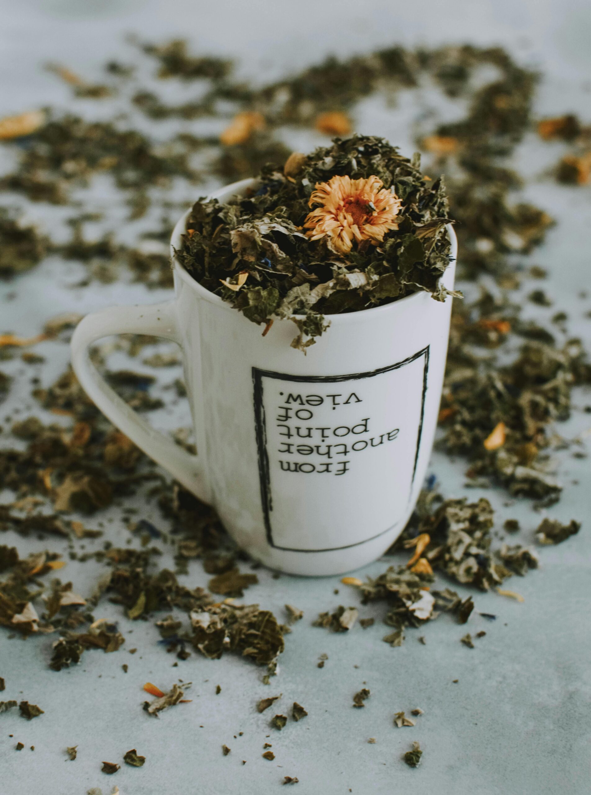 A close-up of an herbal tea mug filled with dried leaves and flowers on a table.